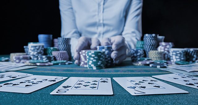 a row of cards of the same suit and a dealer pushing 3 stacks of casino tokens towards the viewer