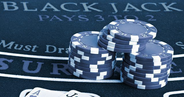 3 stacks of casino tokens on a blackjack online real money table next to 2 playing cards