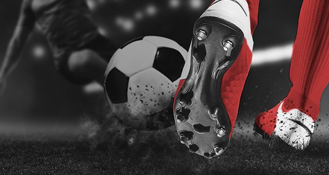 a footballer with red shoes and socks kicking a football