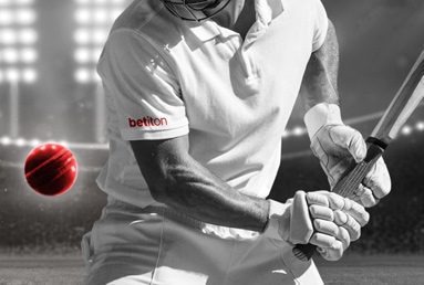 batsman with a betiton branded shirt about to hit a red cricket ball