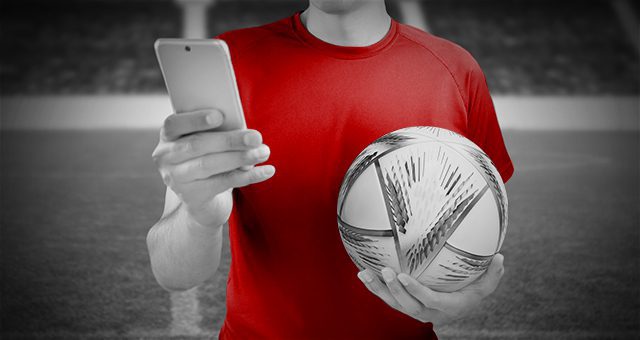 jemand, der den WM-Ball in der Hand hält und dabei ein Smartphone benutzt