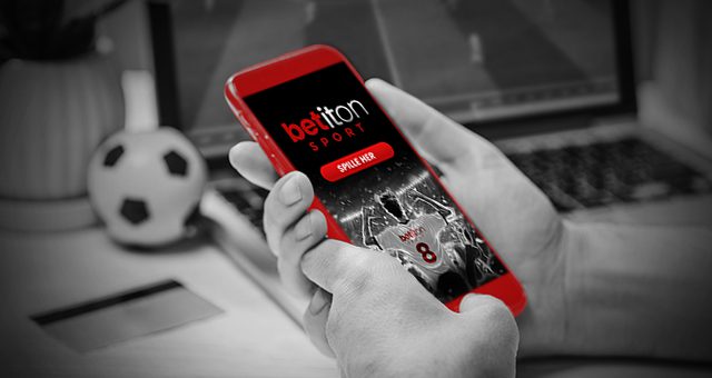 jemand auf seinem Handy auf der Betiton Sport-Website mit einer Schaltfläche Hier spielen